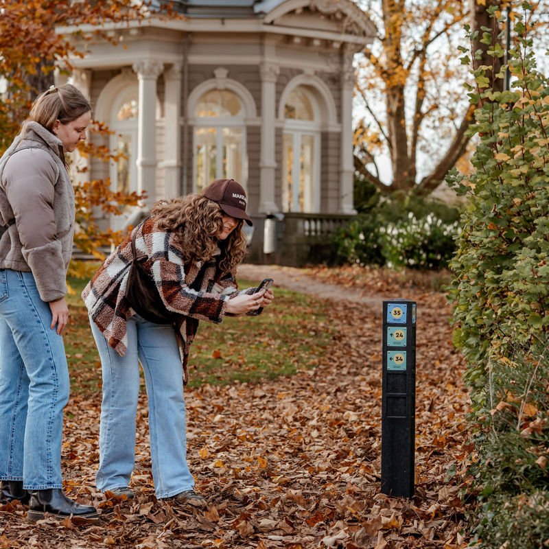 Twee jonge vrouwen scannen QR-code op knooppuntenpaaltje in Proosdijpark in Meerssen in de herfst