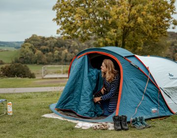 Jonge vrouw opent tent op camping en kijkt naar het heuvellandschap. 