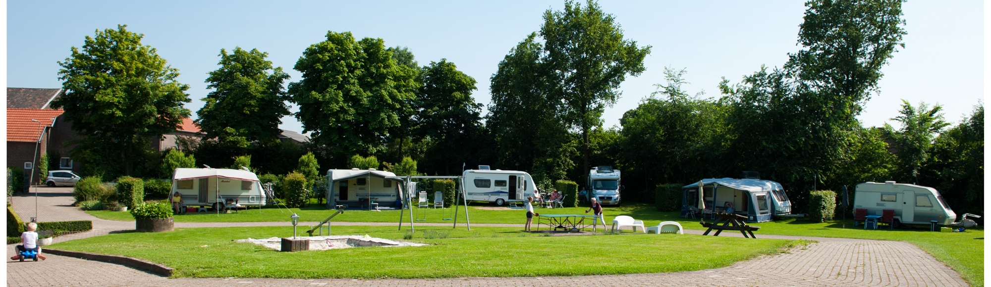 Vlakke weide met gras en enkele caravans.