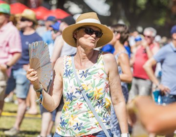 Vrouw met rieten hoed, zonnebril en waaier geniet op het festival terrein
