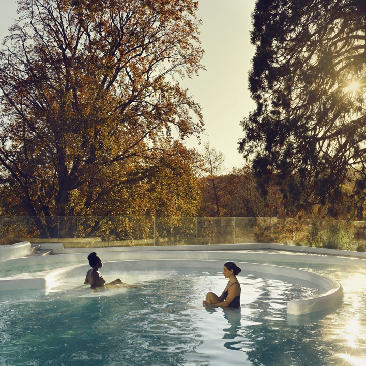 Twee dames zitten in thermaal buitenbad met uitzicht over de herfstige kleuren van de natuur