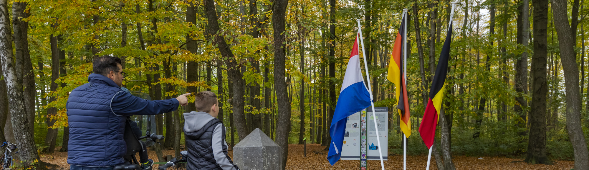 Een vader en zoon wijzen naar de drie nationale vlaggen op het Drielandenpunt