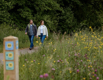 Man en vrouw wandelen langs een grasveld met bloemen en knooppuntenpaaltje