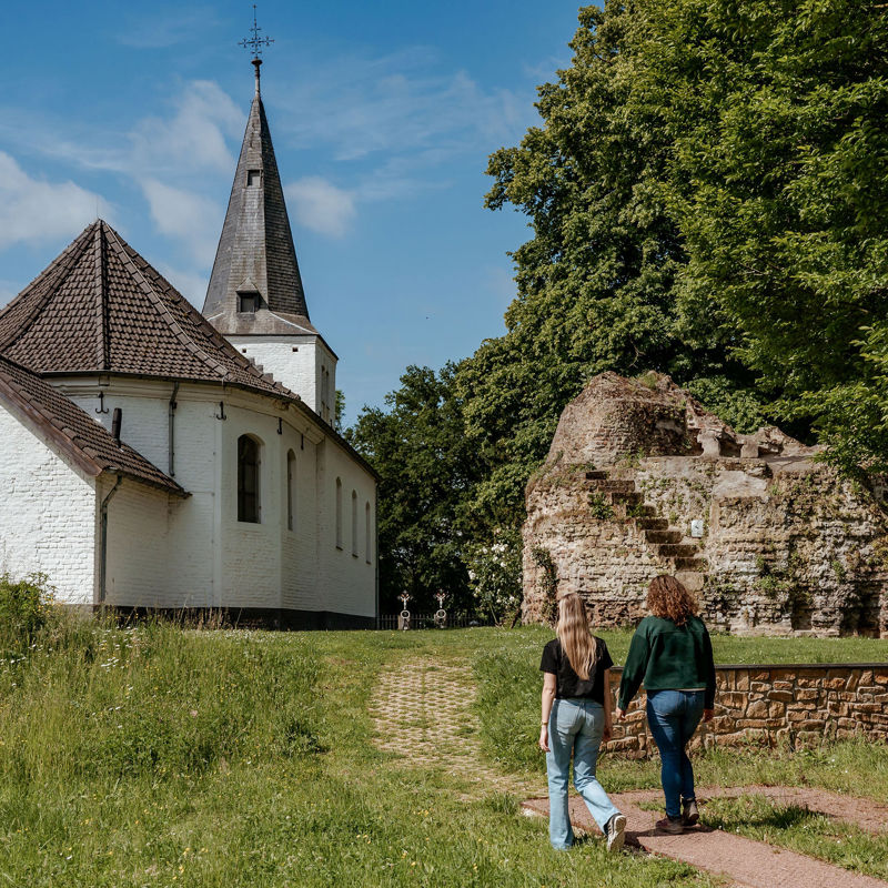 Twee dames wandelen richting een klein wit kerkje. 