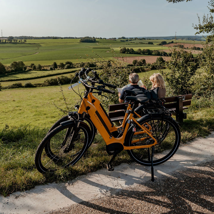Koppel heeft pauze op een bankje met een mooi uitzicht over het zuid-limburgse heuvelland en bekijken de fietskaart met fietsknooppunten. 