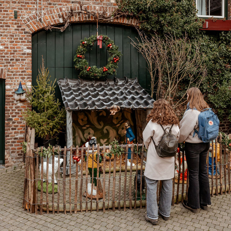 Twee dames met rugzak kijken naar een kerststalletje achter een hekje op een binnenplaats in Mechelen.